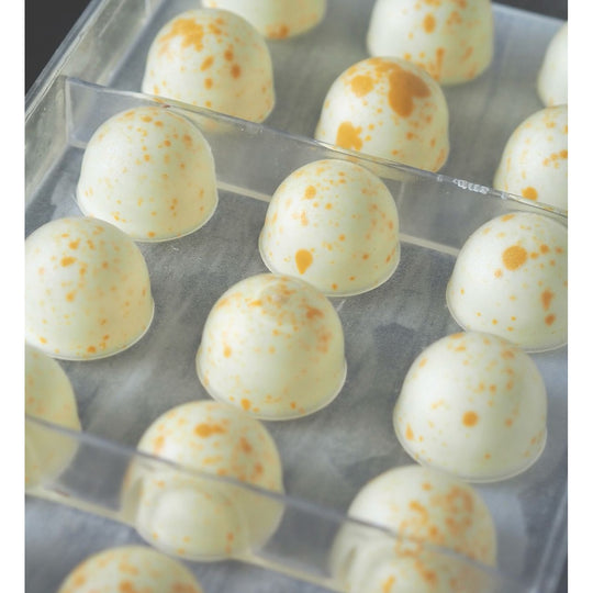 Nærbillede af hvide Callebaut W2 chokoladepraliner med orange prikker i plastform