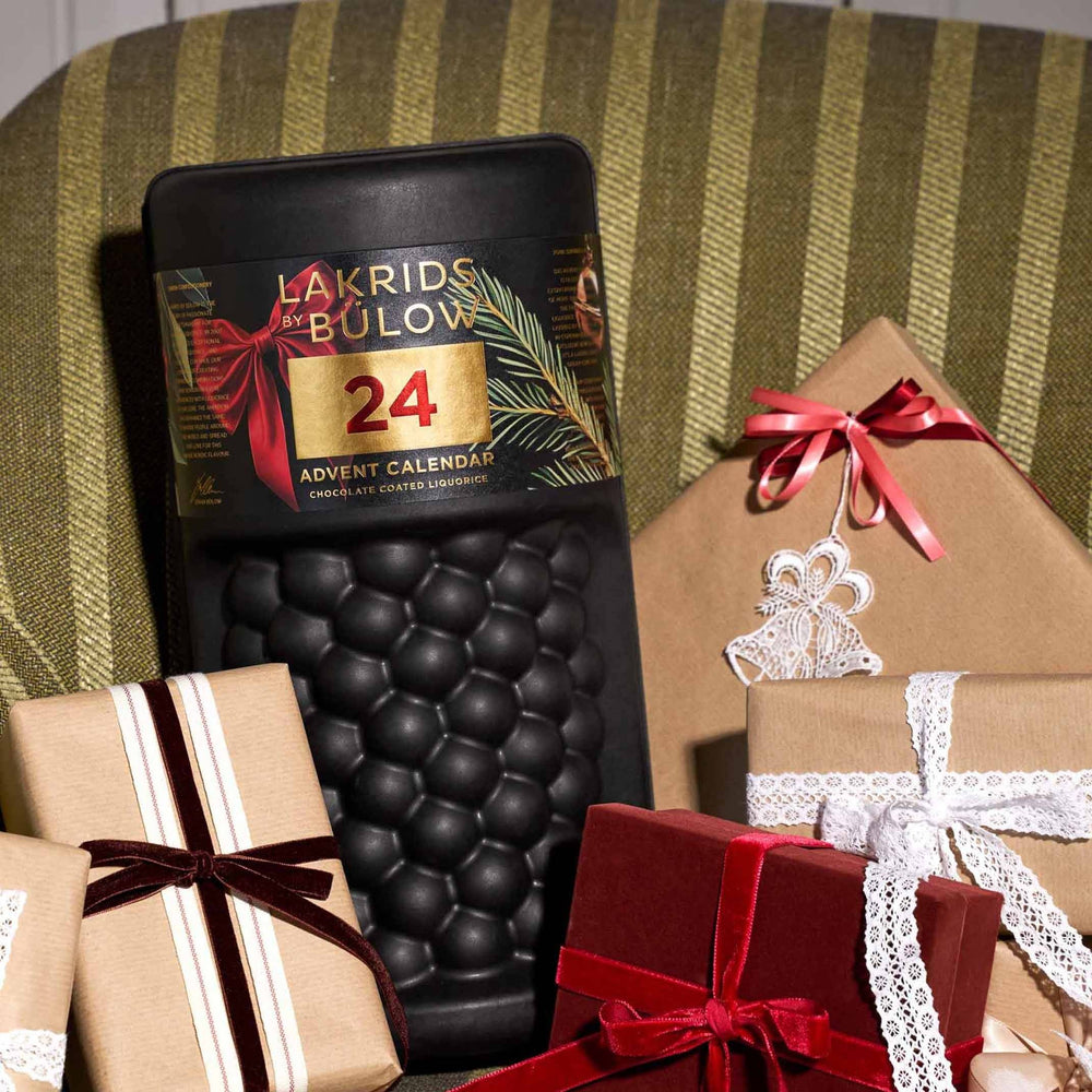 Chokladshopen Lakrids By Bülow stor adventskalender i svart burkdesign omgiven av vackert inslagna julklappar.