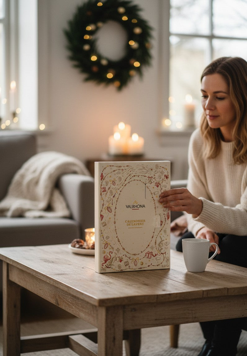 Chokladshopen Valrhona julkalender med festliga illustrationer på ett träbord i ett mysigt vardagsrum med ljus.