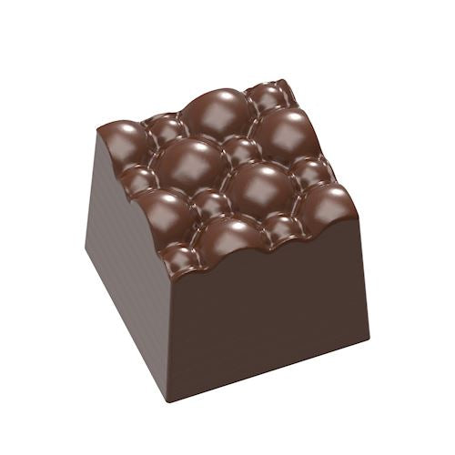 Skinnende mørkebrun chokoladepraline med tydelig boblestruktur og skrå sider